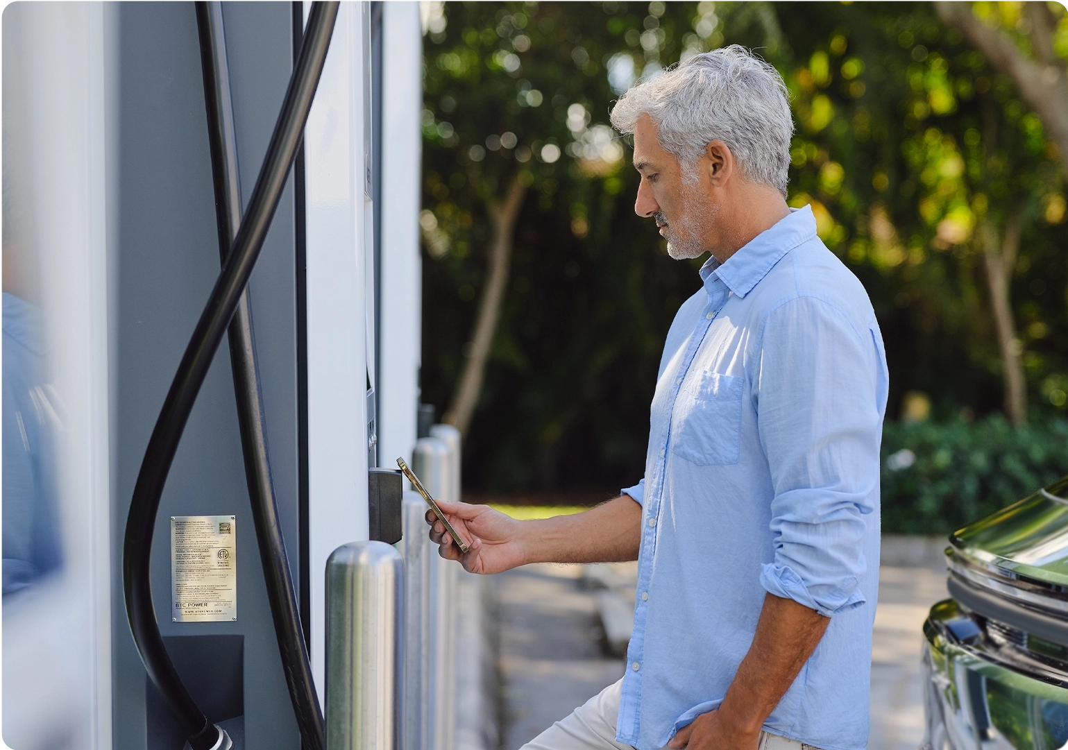 This image displays a person holding their phone up to an NFC reader on an Electrify America charger.