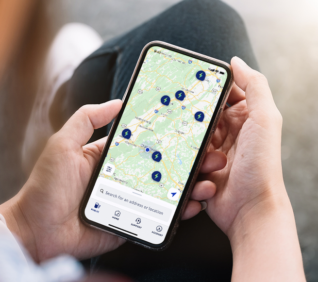 This image displays a person holding their phone up to an NFC reader on an Electrify America charger.