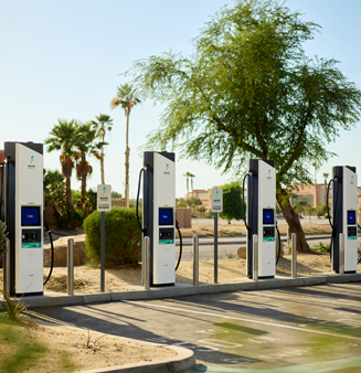 A group of Electrify America fast chargers glowing green at night.