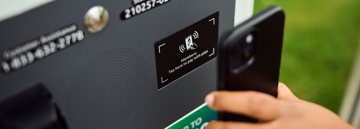 Closeup of a person tapping their phone to pay at an Electrify America charging station.