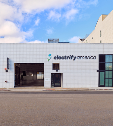 A group of Electrify America fast chargers in a tree-lined shopping center.